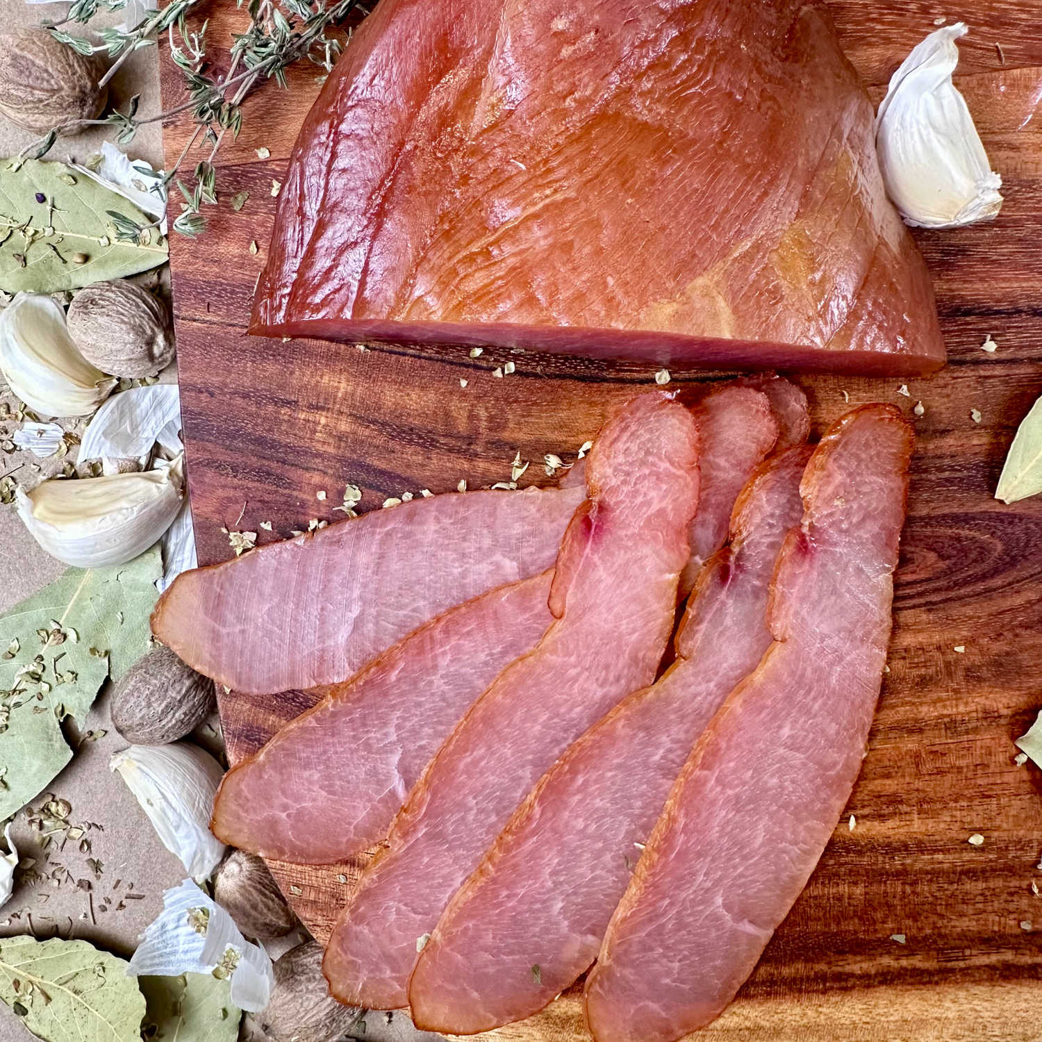 Sliced cured meat on a wooden cutting board with herbs and spices.