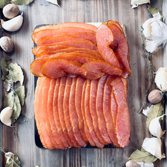 Sliced ham on a wooden board with herbs and garlic cloves.