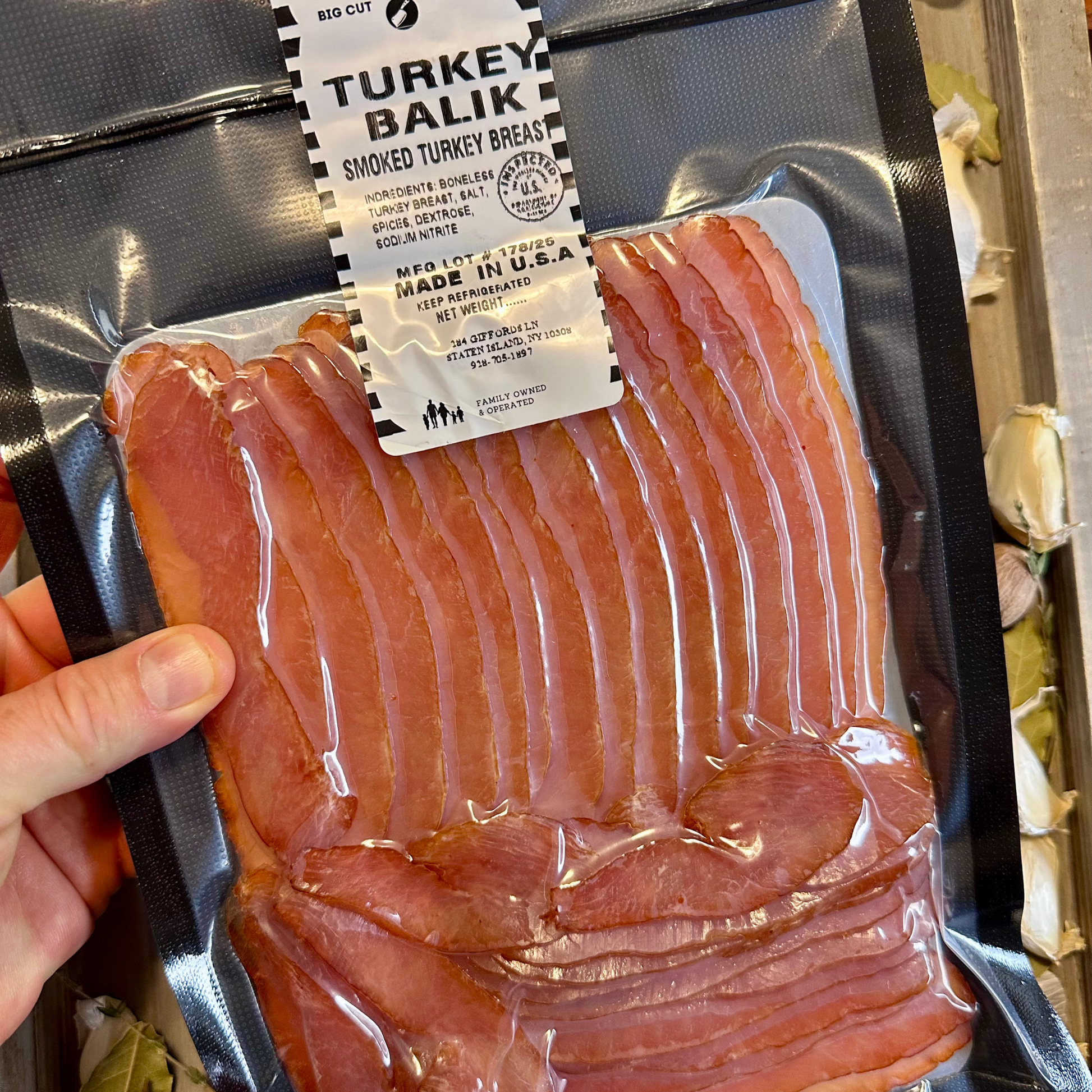 Packaged smoked turkey breast with a label held by a hand.