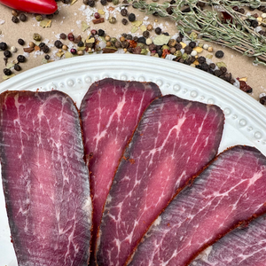 Thin slices of air-dried basturma beef on a white plate with herbs and spices – Papa Did It