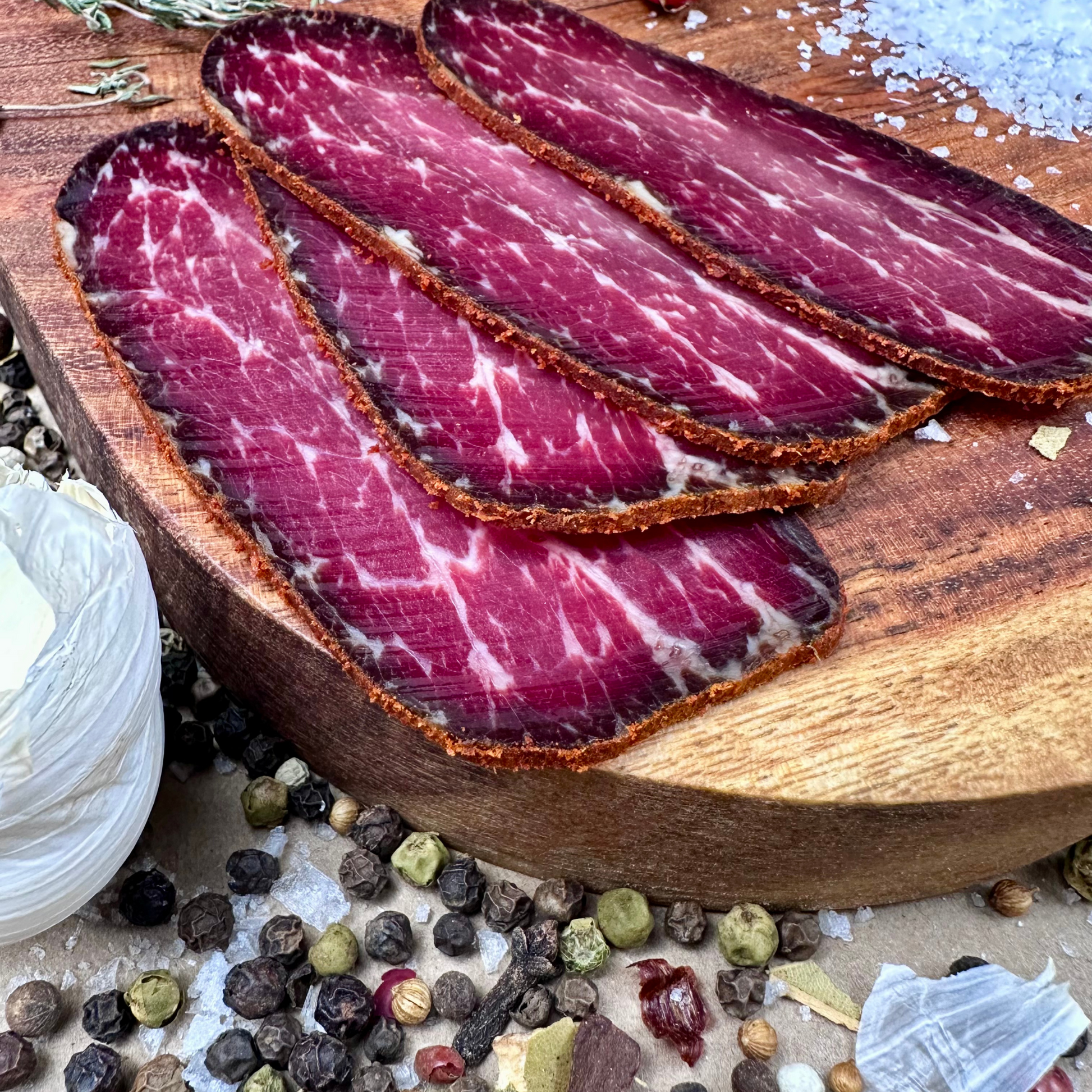 Thin slices of Papa Did It basturma air-dried beef on wooden board with garlic and spices