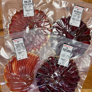 Four vacuum-packed meat products including sliced basturma, turkey balyk, pork loin with herbs, and beef prosciutto.
