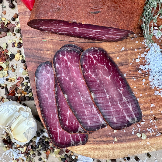 Sliced basturma smoked beef on wooden board with garlic, herbs, and spices – Papa Did It handcrafted meat