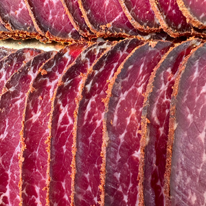 Close-up of sliced cured meat with a reddish-pink color and visible fat marbling.