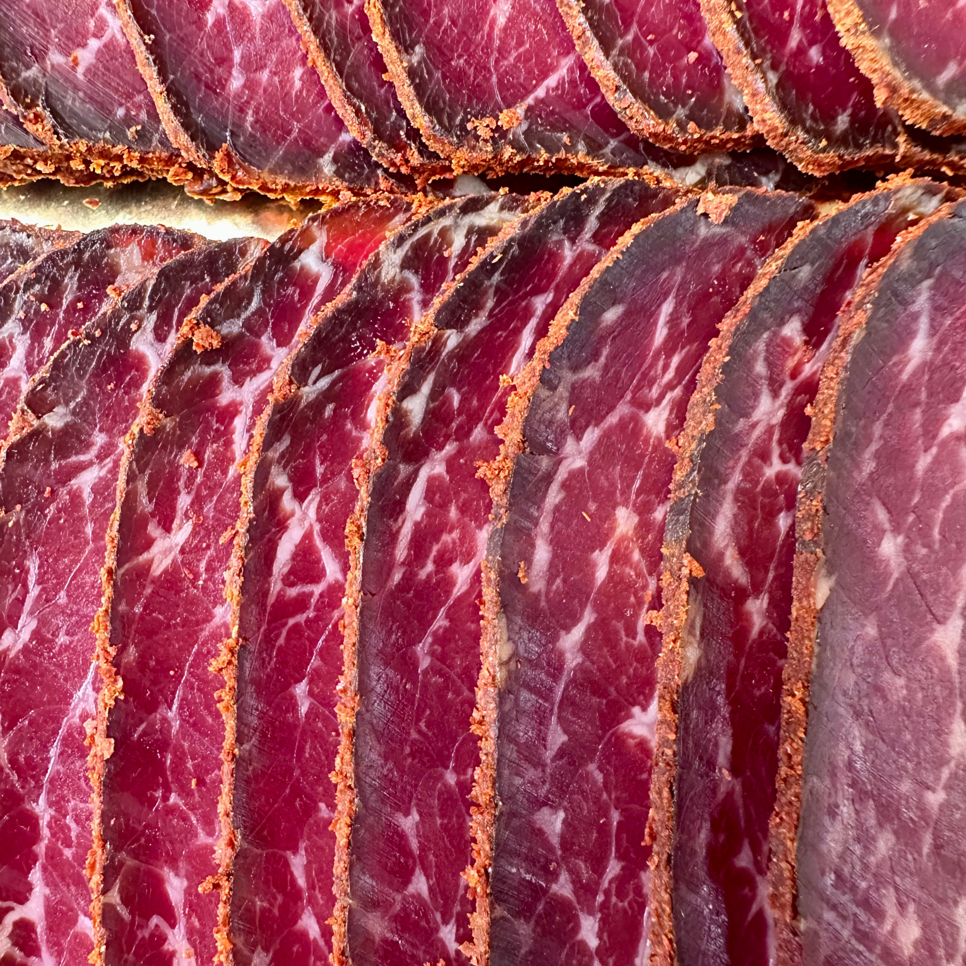 Close-up of sliced cured meat with a reddish-pink color and visible fat marbling.