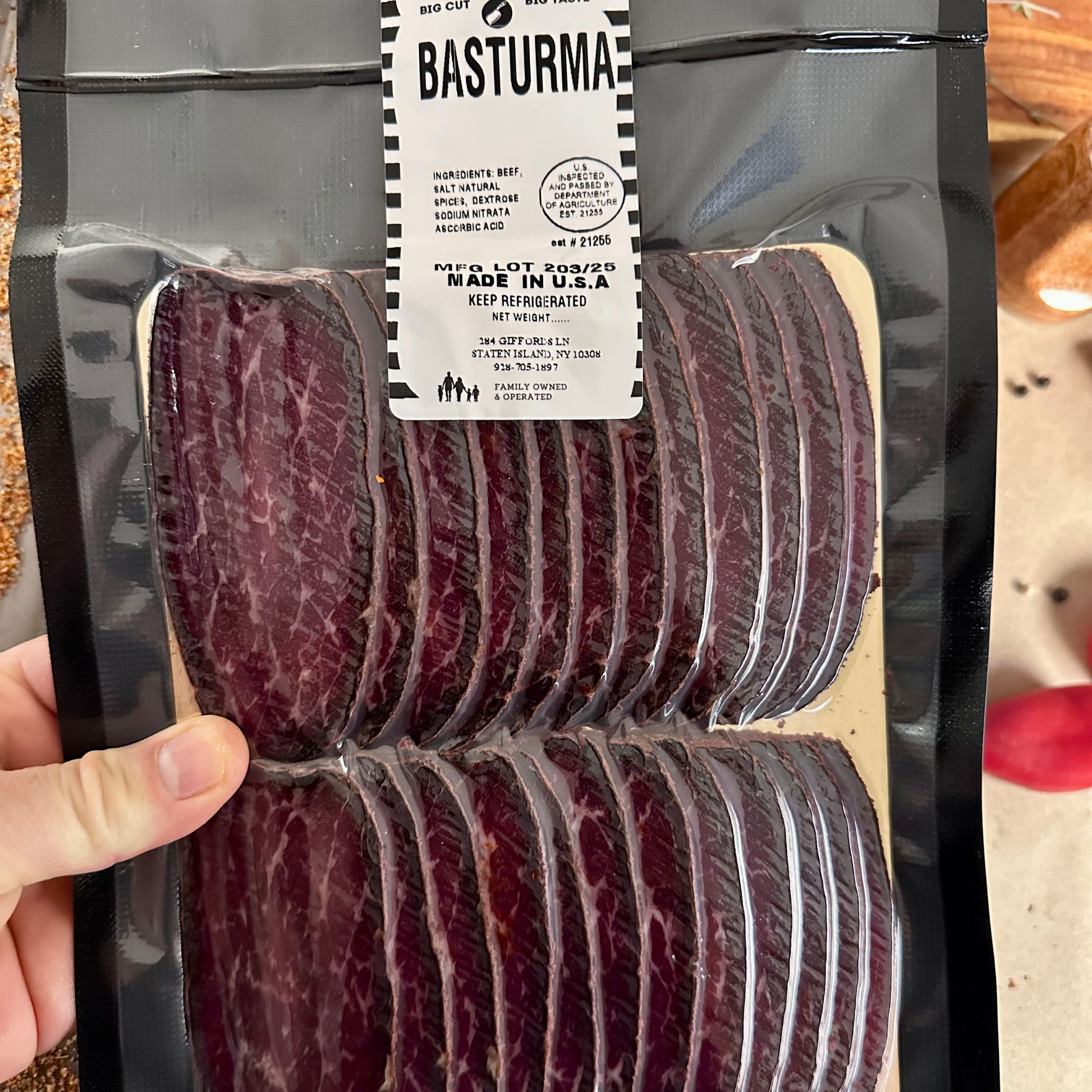Packaged beef jerky with a 'Basturma' label held by a hand.