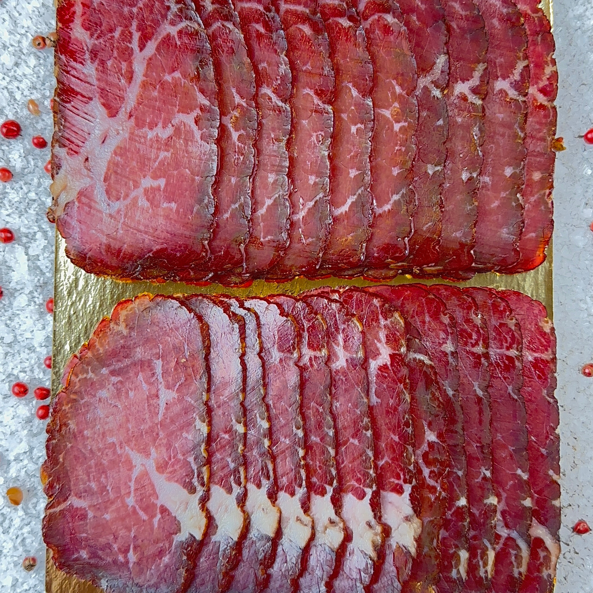 Thinly sliced red cured beef displayed on a golden tray with pepper and salt around
