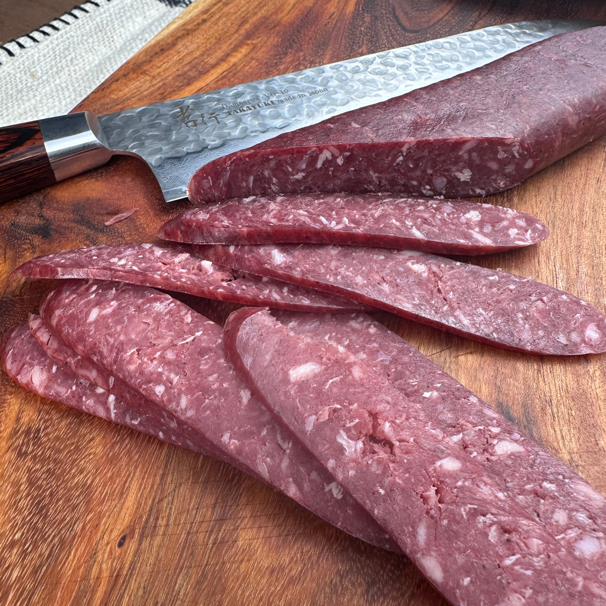 Thinly sliced beef sudjuk sausage on a wooden board with a knife