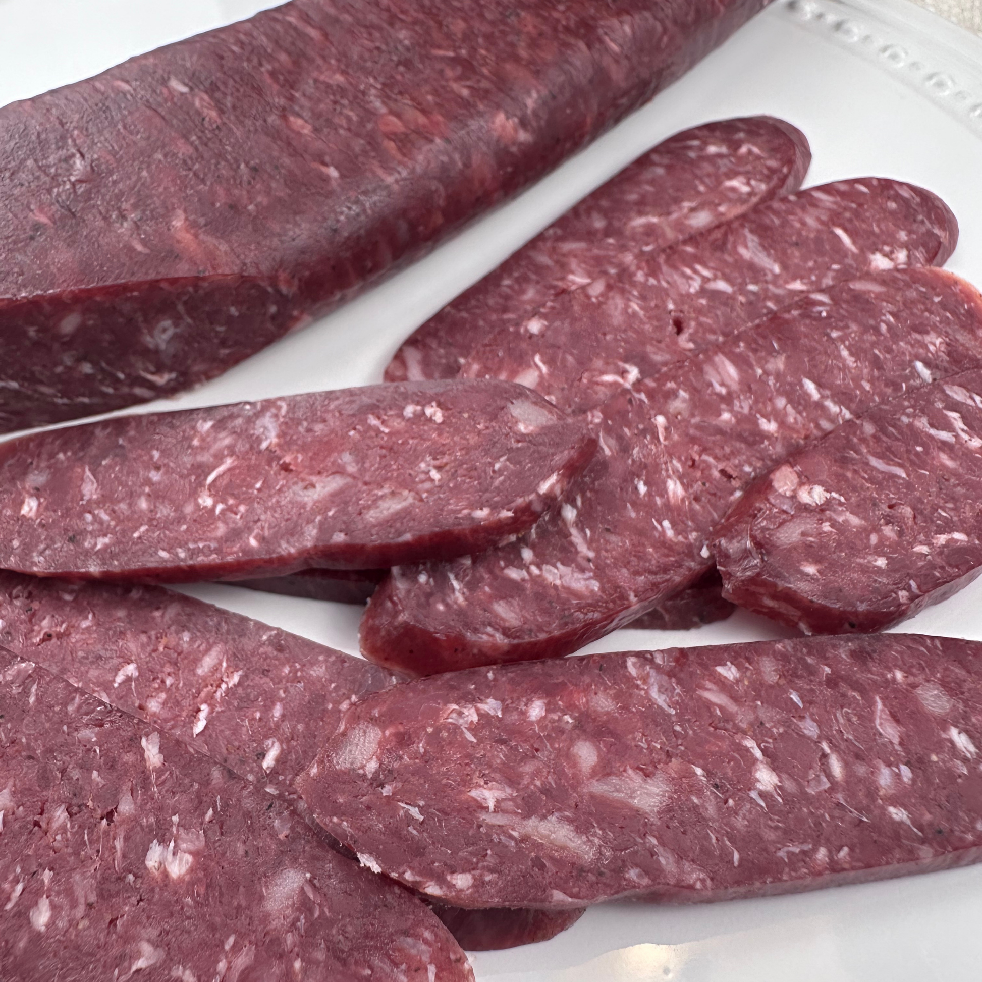 Whole and sliced beef sudjuk served on white plate