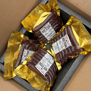 papa did it beef sticks box packaging — four vacuum-sealed packs of handcrafted hickory-smoked beef sticks in golden wrapping neatly arranged inside an insulated shipping box, ready for delivery from Papa Did It