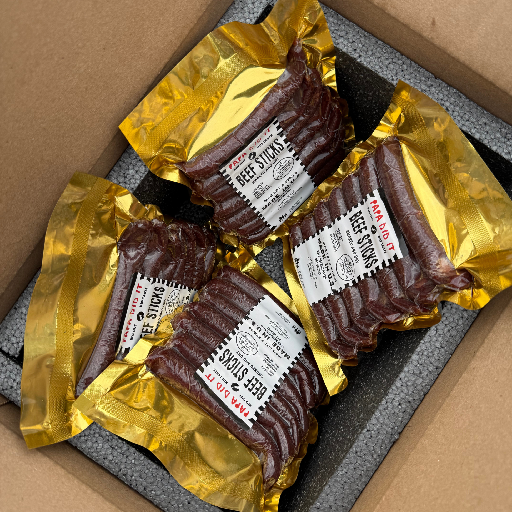 papa did it beef sticks box packaging — four vacuum-sealed packs of handcrafted hickory-smoked beef sticks in golden wrapping neatly arranged inside an insulated shipping box, ready for delivery from Papa Did It