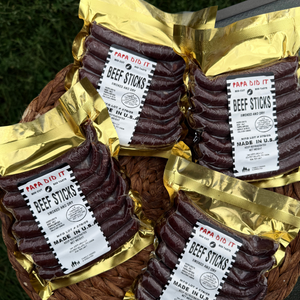 Papa Did It Beef Sticks — four golden vacuum-sealed packs of handcrafted hickory-smoked beef sticks displayed in a rustic basket. Premium dry-cured meat snack made in the USA.