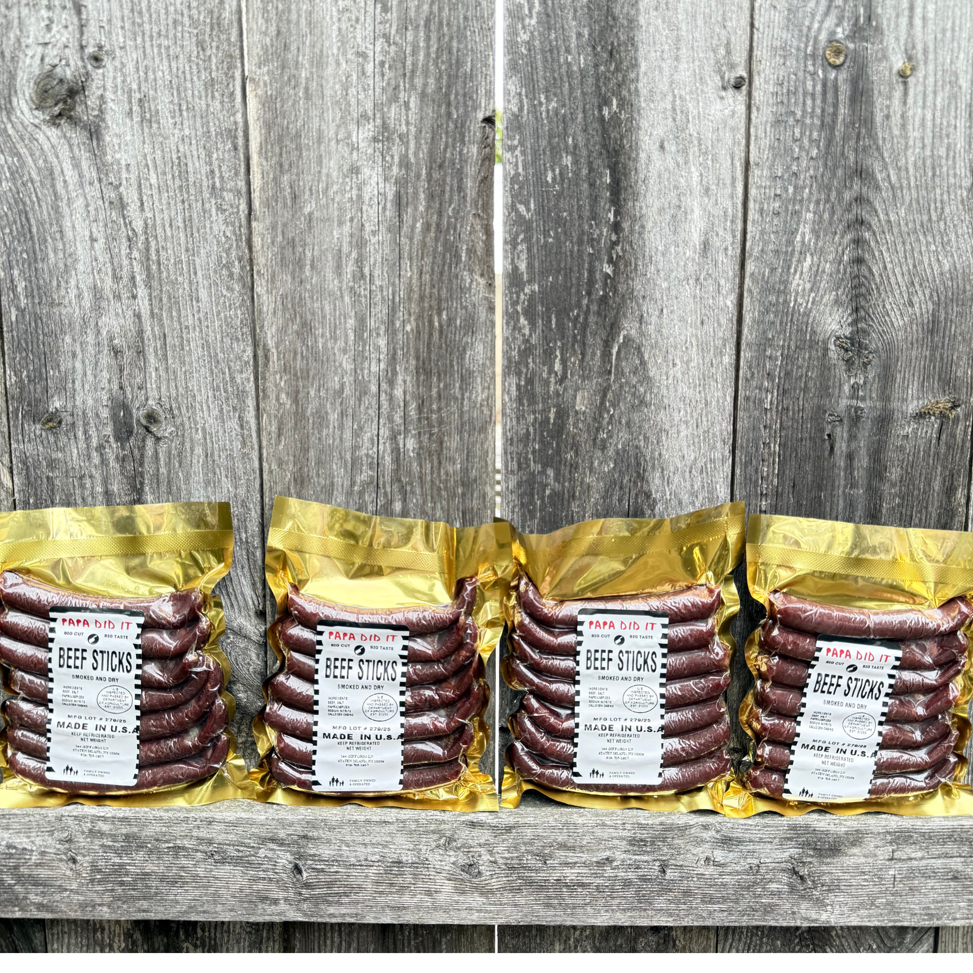 papa did it beef sticks lineup on wooden background — four golden vacuum-sealed packs of handcrafted hickory-smoked beef sticks made in the USA, displayed neatly against rustic wood for a clean artisan presentation