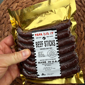 papa did it beef sticks single pack front — close-up of one golden vacuum-sealed pack of handcrafted hickory-smoked beef sticks made in the USA, held by hand on a woven surface showing the product label clearly
