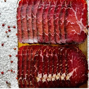 Close-up of thinly sliced beef prosciutto on a golden board with sea salt and peppercorns — handcrafted hickory-smoked beef by Papa Did It.

