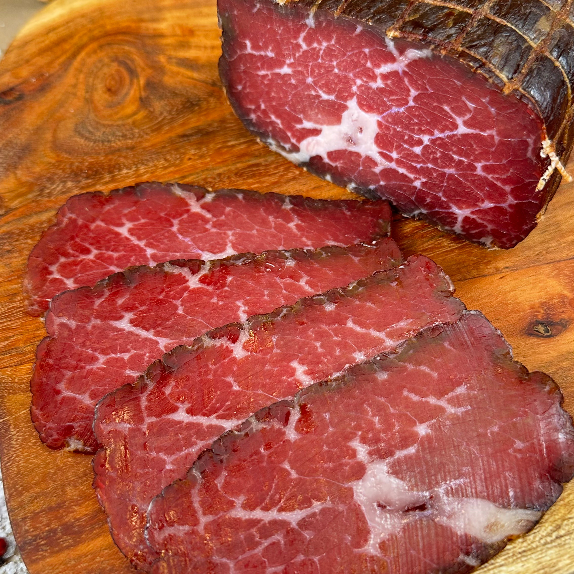 Sliced hickory-smoked beef prosciutto on a wooden board — handcrafted dry-cured beef by Papa Did It.