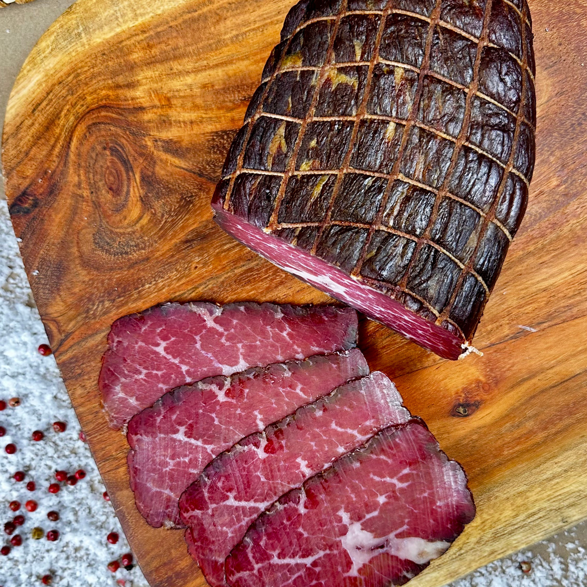 Half-cut hickory-smoked beef prosciutto with thin slices on a wooden board — handcrafted dry-cured beef by Papa Did It.