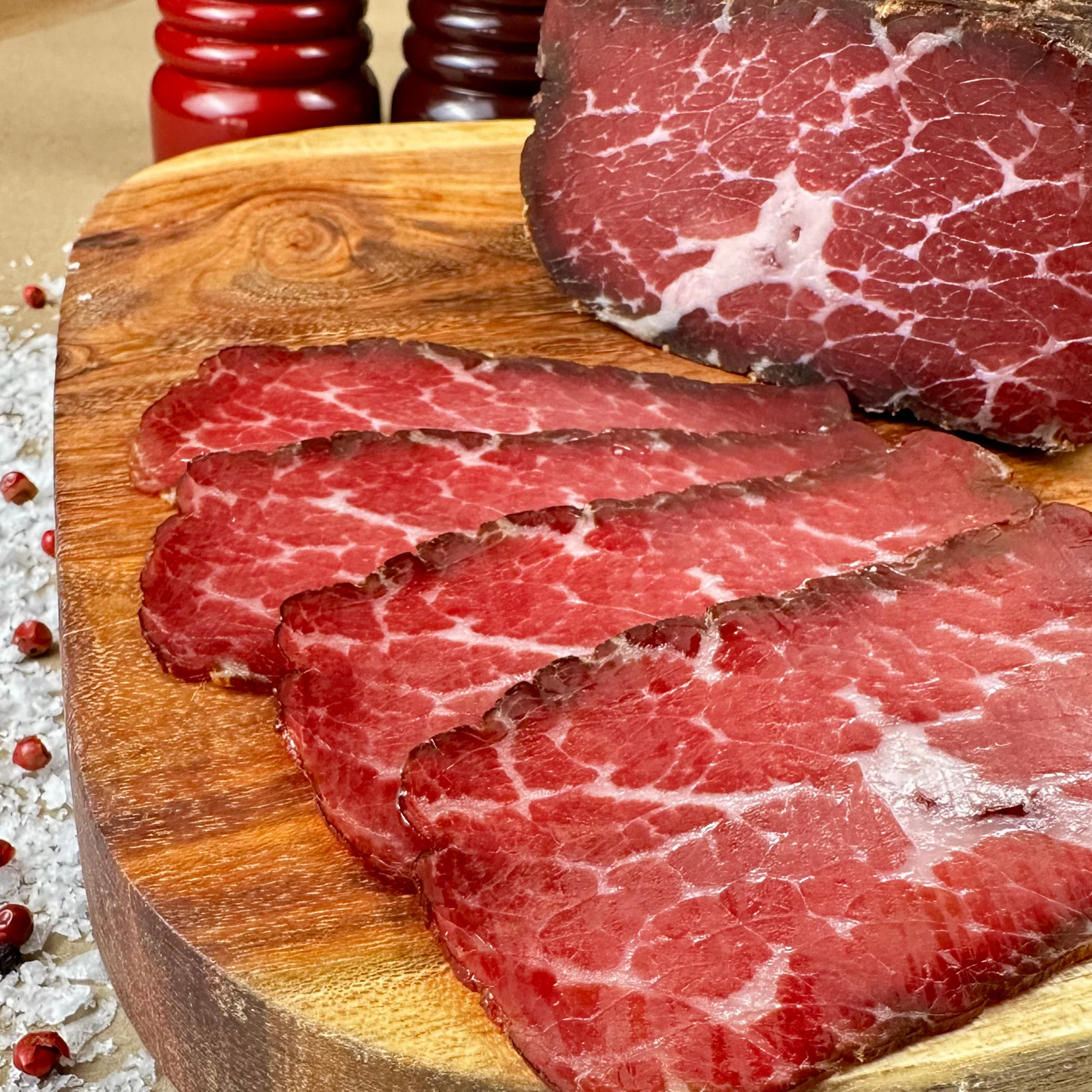 Thin slices of hickory-smoked beef prosciutto on a wooden board — rich marbling and deep red color, handcrafted by Papa Did It.
