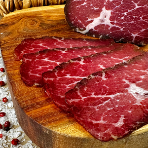 Thin slices of hickory-smoked beef prosciutto on a wooden cutting board
