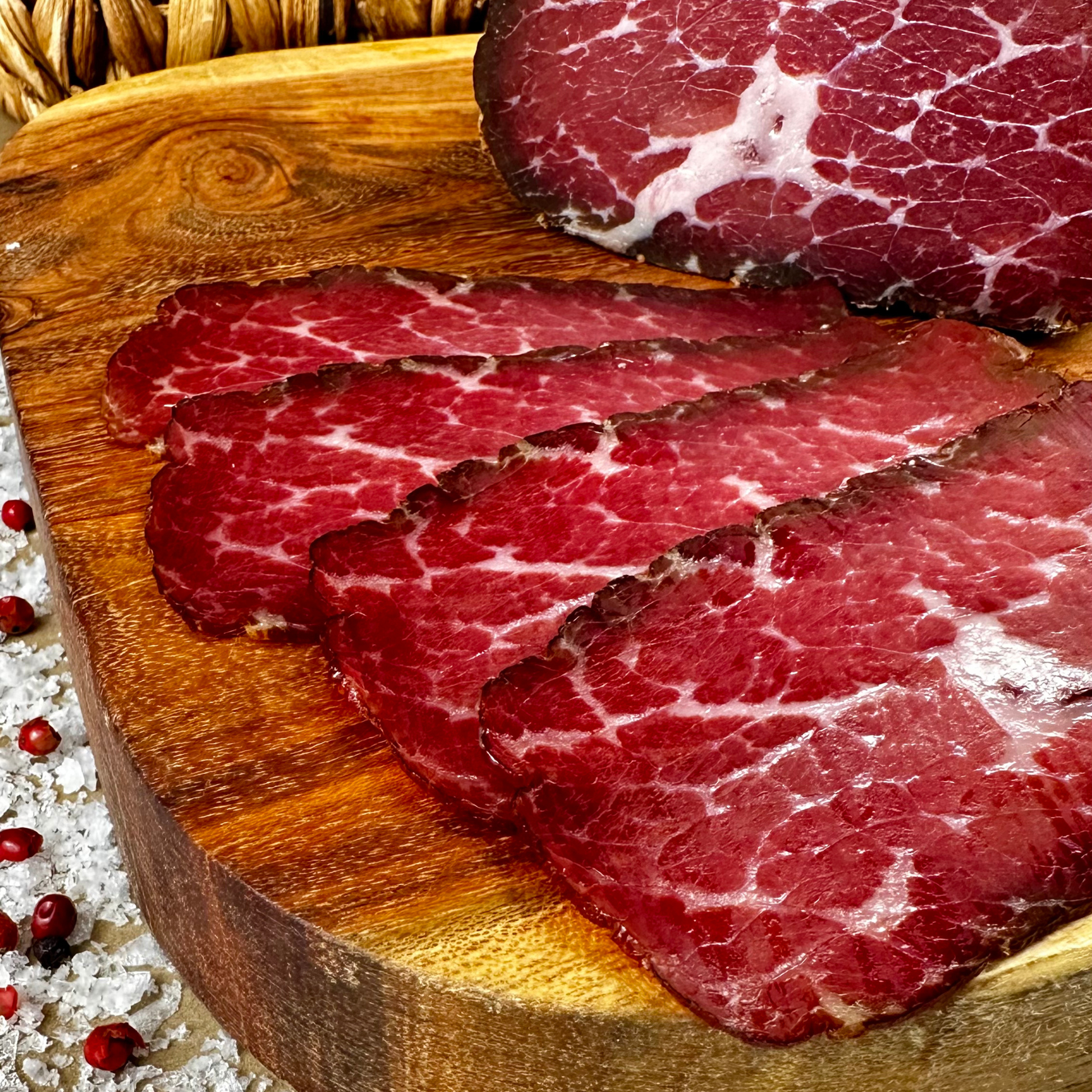 Thin slices of hickory-smoked beef prosciutto on a wooden cutting board
