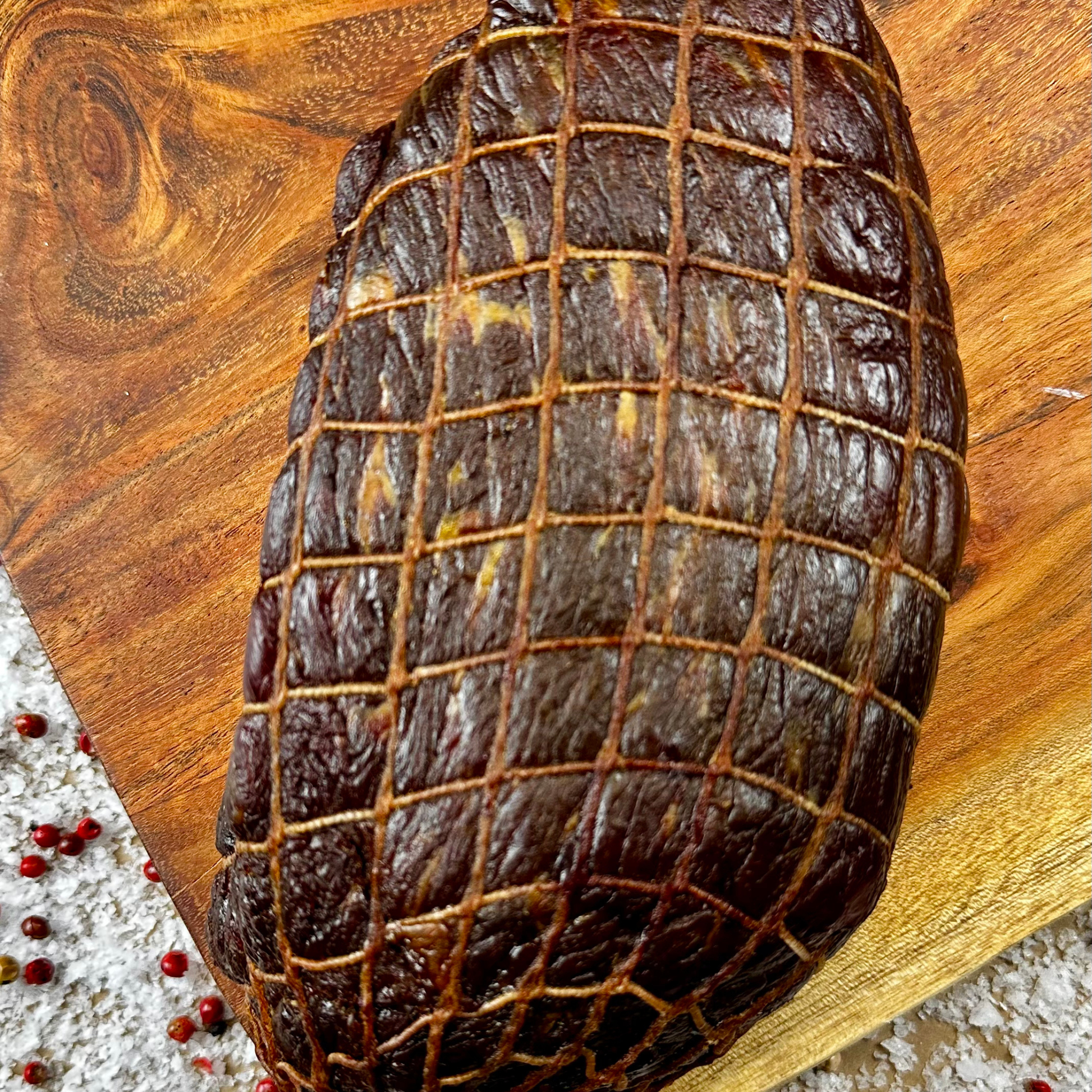 Whole hickory-smoked beef prosciutto piece with dark dry-cured crust on a wooden board — handcrafted by Papa Did It.
