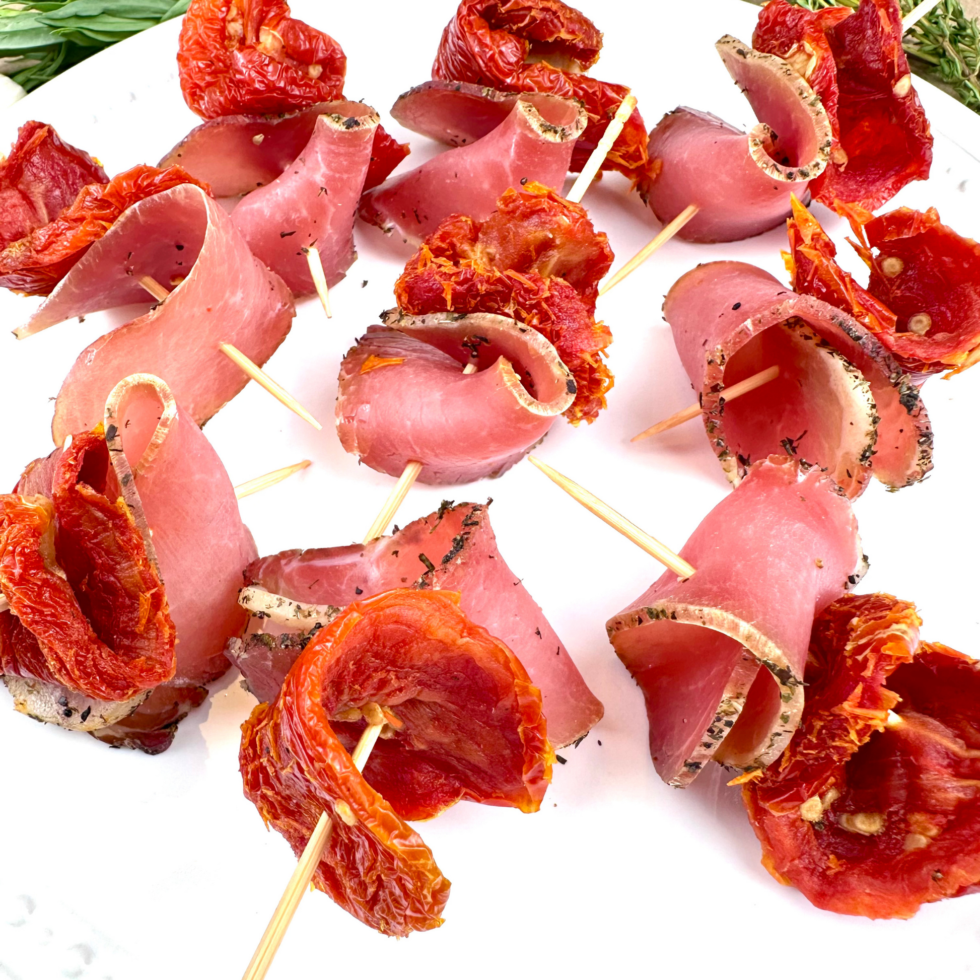 Herb-smoked pork loin slices with sun-dried tomatoes on skewers