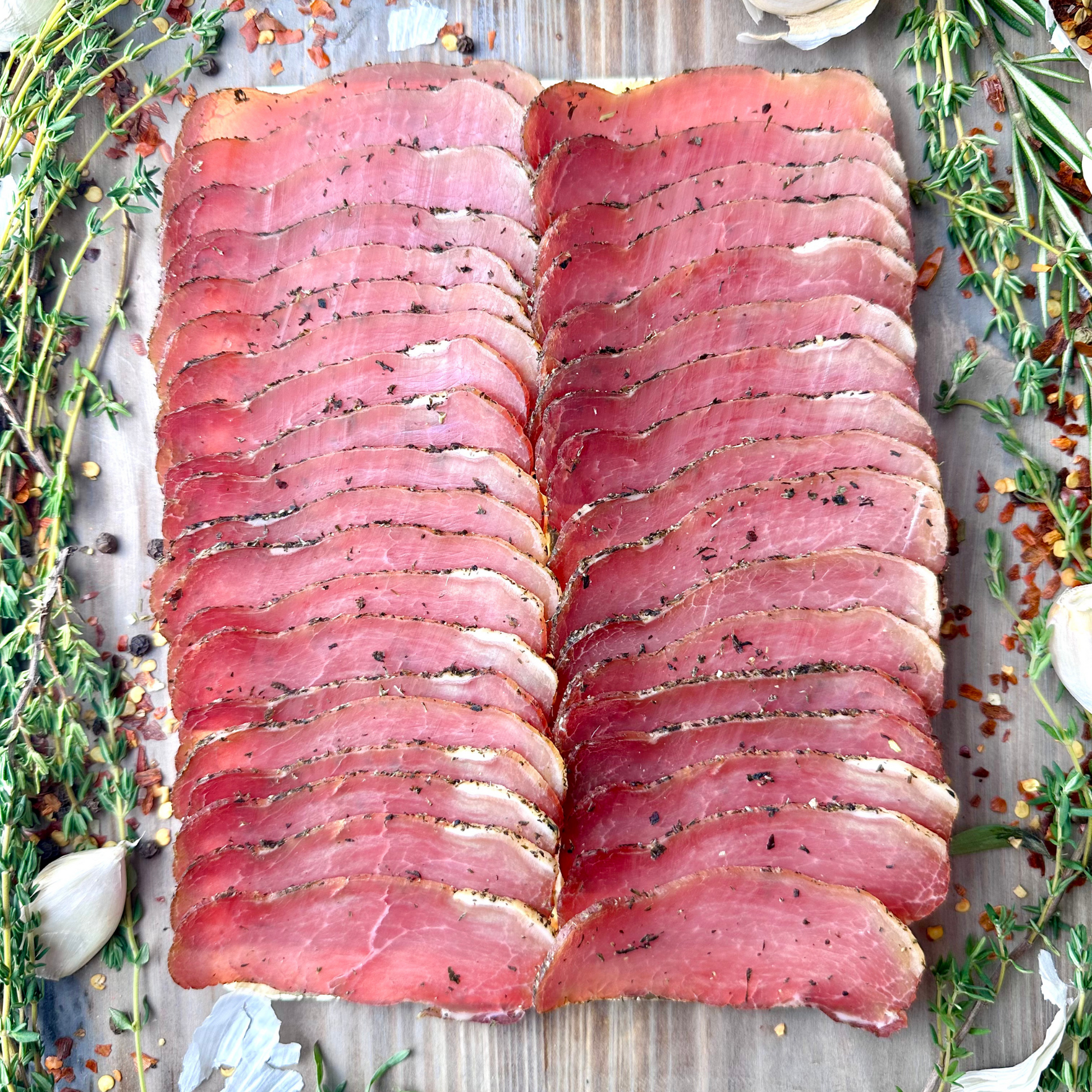 Thinly sliced pork loin with herbs arranged on platter with garlic and spices