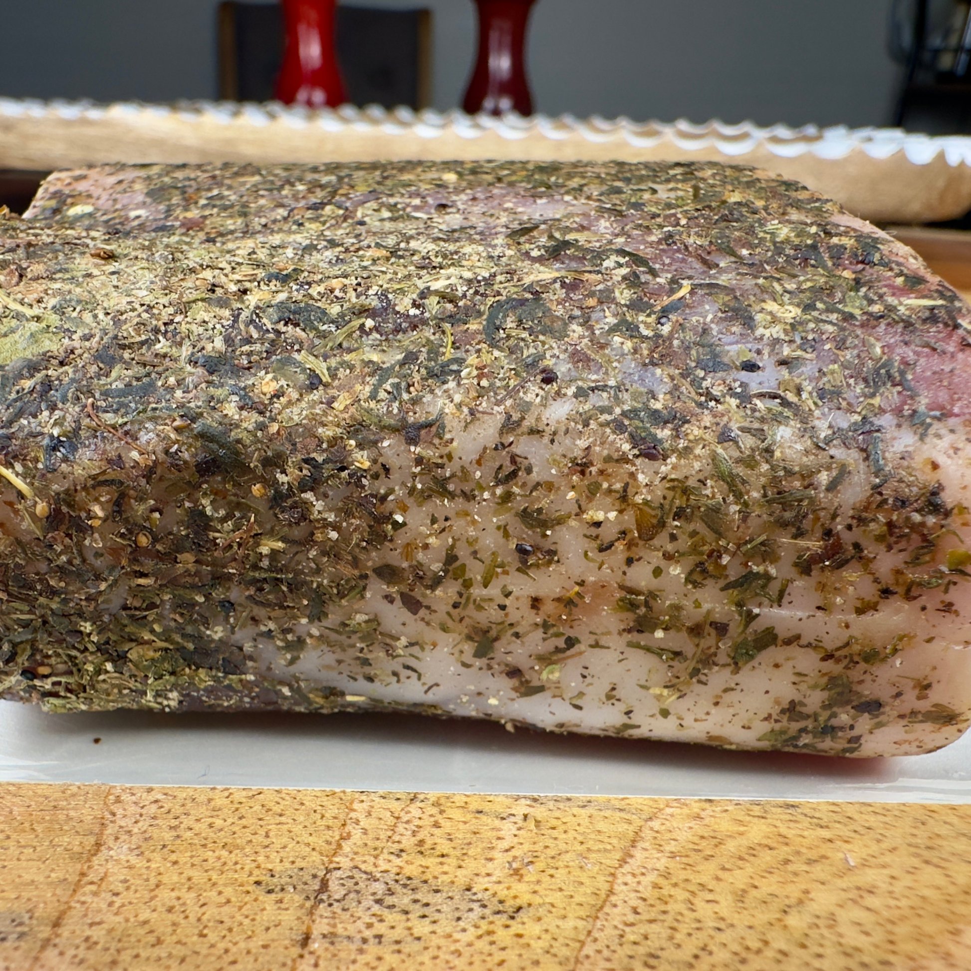 Whole dry-cured pork loin crusted with herbs on a wooden board