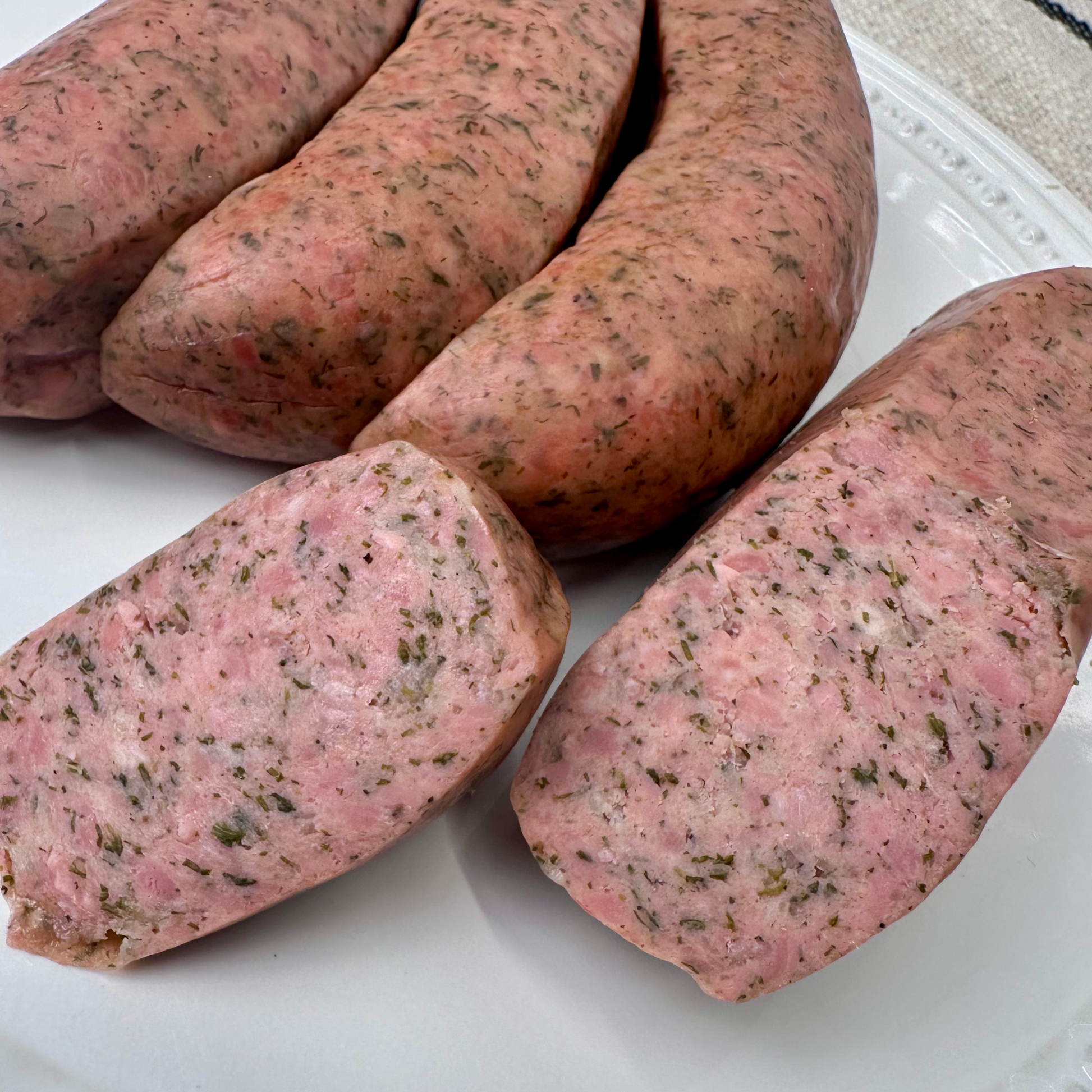Close-up of sliced savory grilled chicken sausages with dill and garlic on a white plate