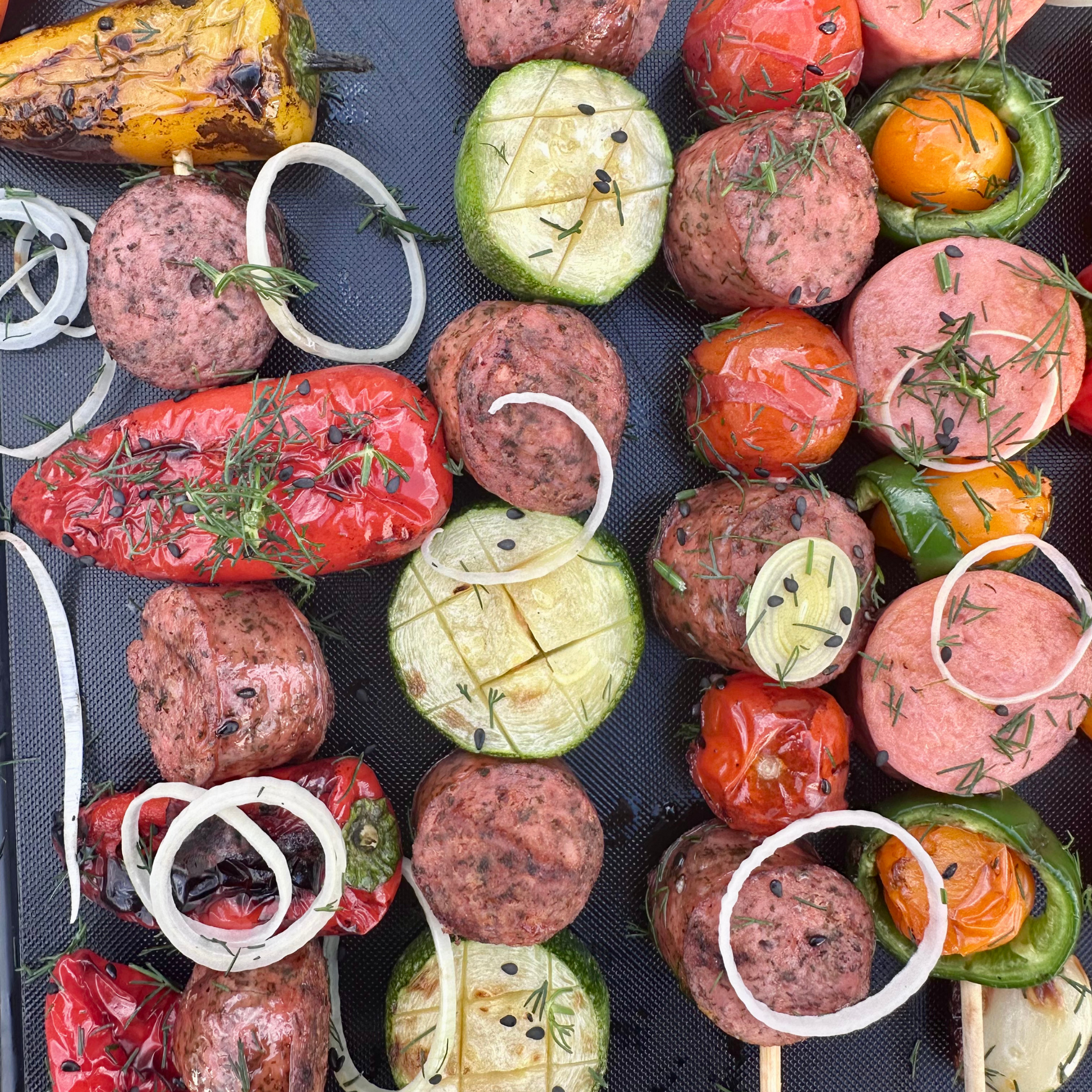 Grilled chicken sausage skewers with fresh vegetables, onions, peppers, and zucchini on a grill mat
