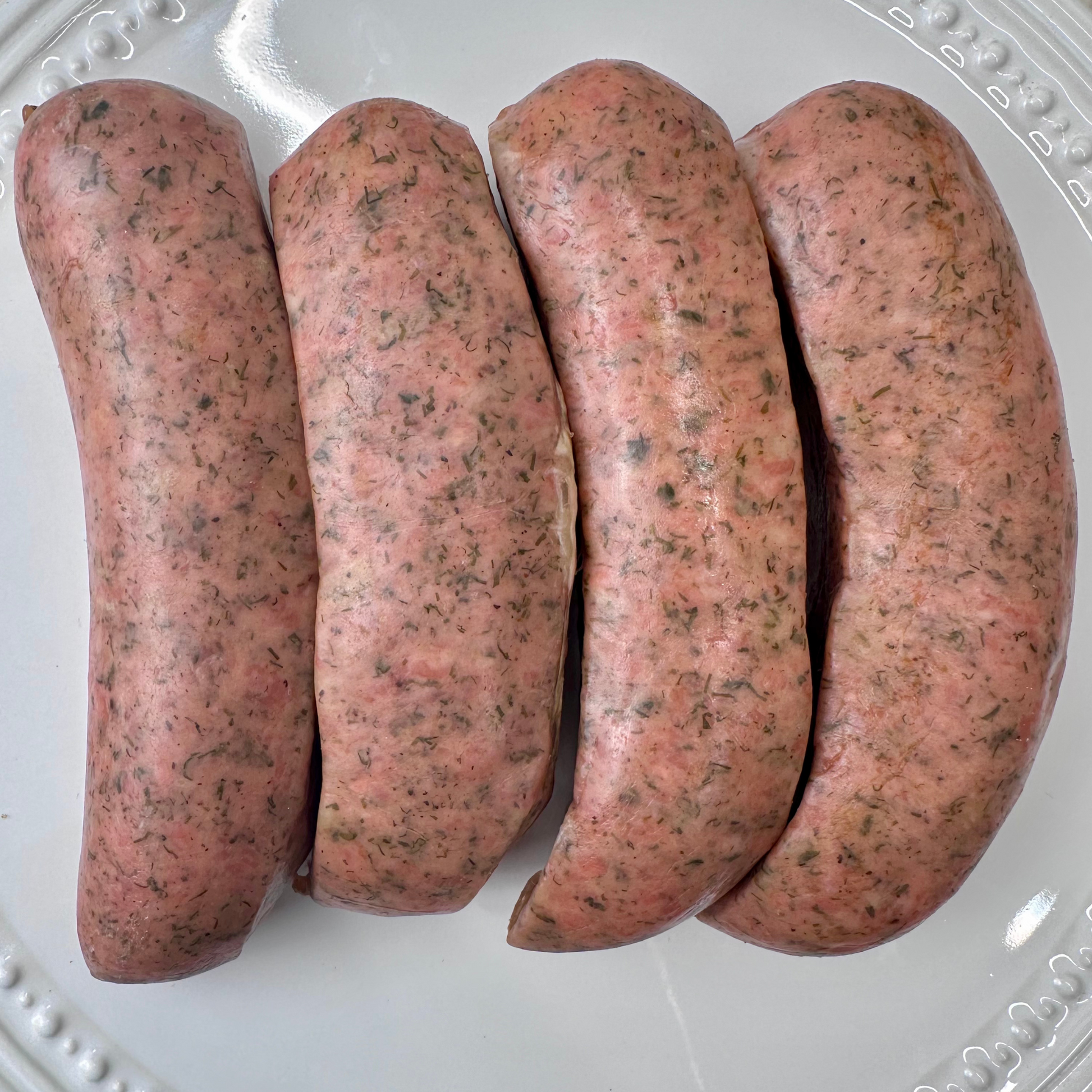 Uncooked savory chicken grill sausages arranged on a white plate