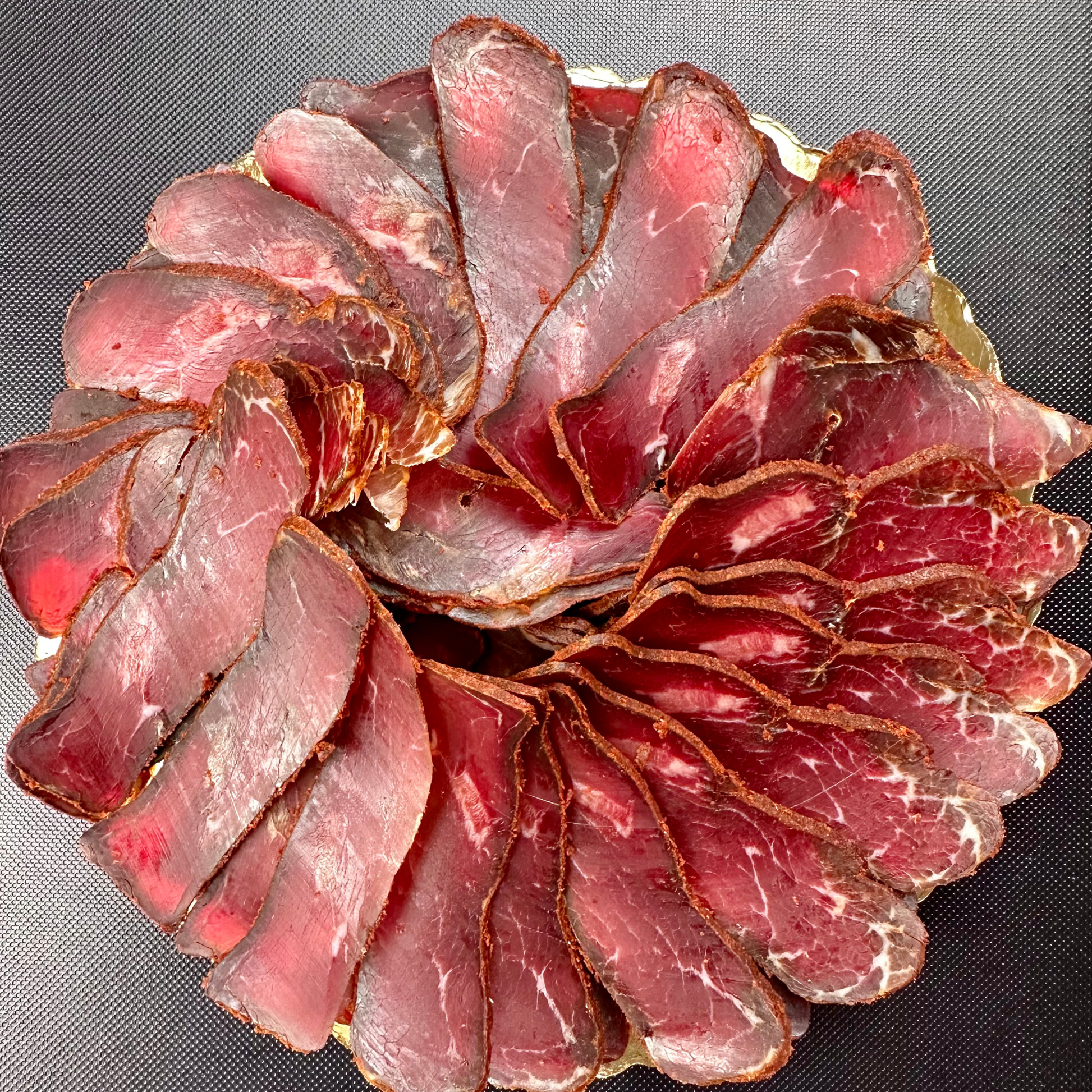 Sliced basturma arranged in a circular charcuterie-style presentation