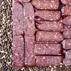 Sliced beef sujuk dry-cured sausage on peppercorn background – artisanal hickory smoked beef slices