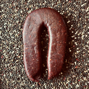 Whole beef sujuk dry-cured sausage in horseshoe shape on peppercorn background – artisanal hickory smoked sausage